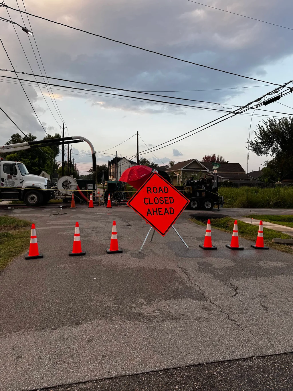 Road Closed Ahead sign and cones beside a utility bucket-truck operation.